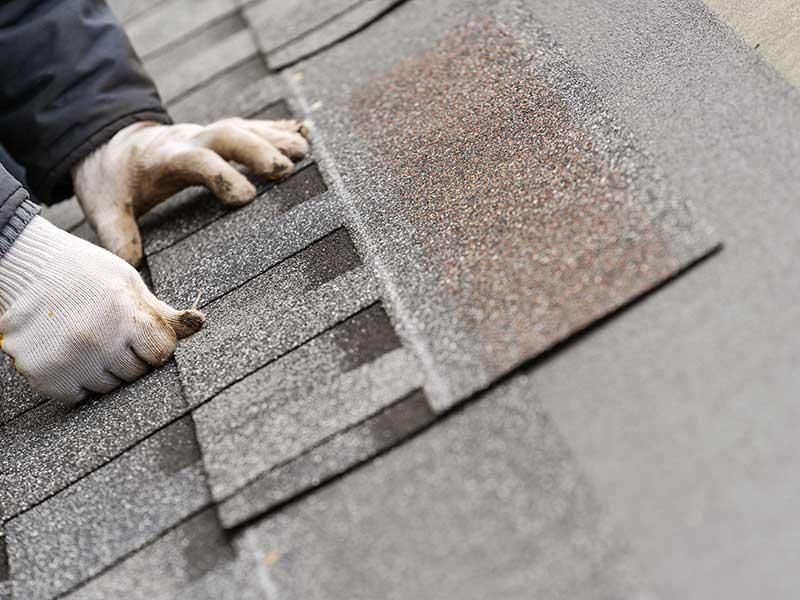 Close-up of a worker's gloved hands placing shingles on a roof, getting it ready to install